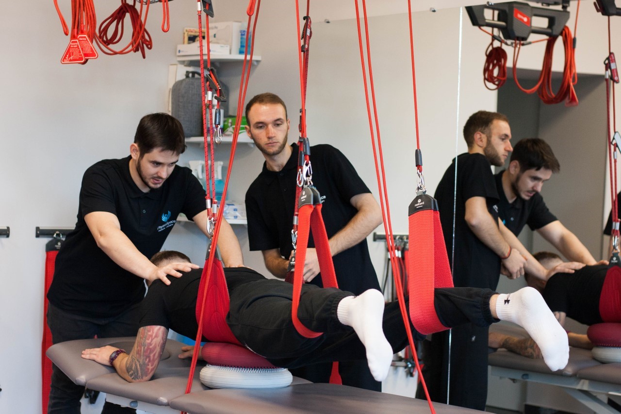 In a gym, two men are doing physical therapy, using the Neurac method to restore movement functions.
