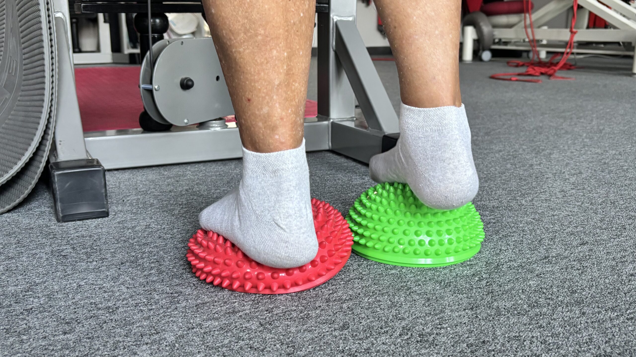 Person in socks and shoes balancing on green and red exercise balls